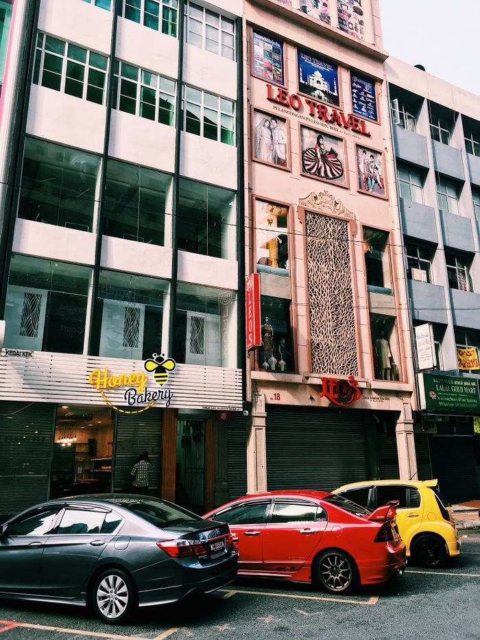 Lively street in Kuala Lumpur, Malaysia with colorful cars parked by shops.